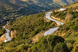 Serpentines of a mountain road with a small church in the highlands of the Greek Cyclades island Andros in the evening light